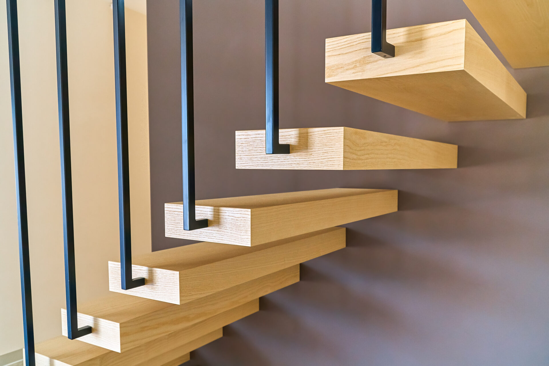 Floating stairs. Ash lumber stairs with metal railing attached to brown wall and leading to second floor inside stylish modern house